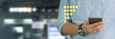Man holding smartphone device and touching screen with five star rating feedback iconの写真素材