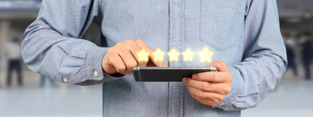 Man holding smartphone device and touching screen with five star rating feedback iconの写真素材