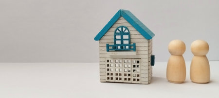 Building a home together wooden figurines next to a miniature house on a white backgroundの写真素材