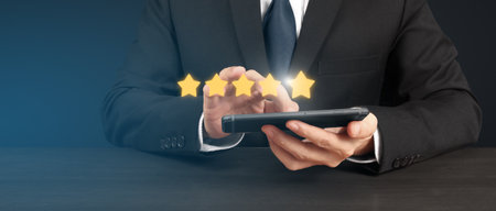 Man holding smartphone device and touching screen with five star rating feedback iconの写真素材