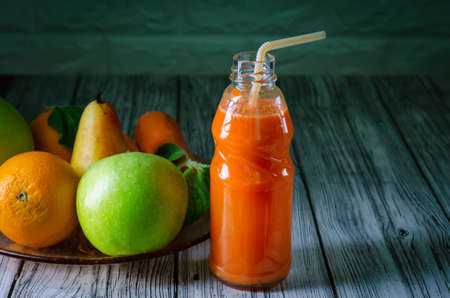 Fresh juice from orange green apple with pears and carrots in a bottle with a straw front view on wooden backgroundの写真素材