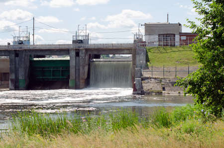 old dam of a power station on a river with green grass in the foreground and a blue sky with cloudsの写真素材