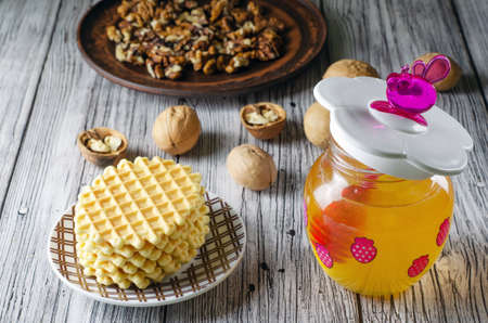 funny baby jar of honey with a pink honey spoon and walnuts and waffle cookies on a wooden tableの写真素材