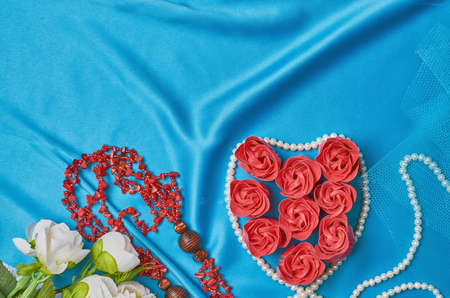 Heart of red flower buds on a blue beautiful fabric with beads of pearls and coral top viewの写真素材
