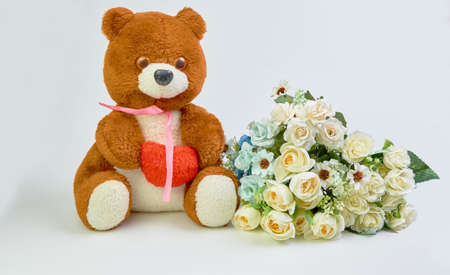 Teddy bear with a red heart in his hands and a bouquet of flowers on a light background with place for text.の写真素材