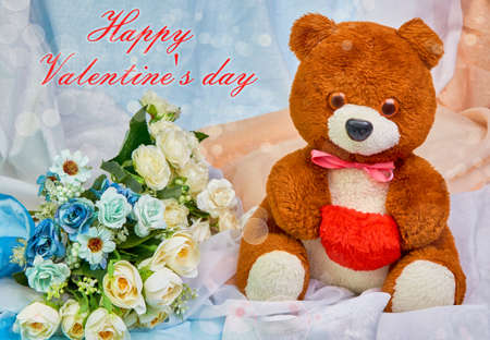 Teddy bear with a red heart in hands and a bouquet of flowers on a colored festive background with text happy valentines day.の写真素材