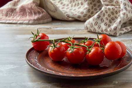 Cherry tomatoes on a green branch lie in a brown clay plate with drops of water. Close-up.の写真素材