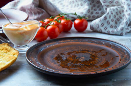 Empty brown clay plate on the table with a gravy boat, cherry tomatoes, bread and a towel in the backgroundの写真素材