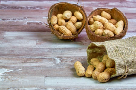 Peanuts lies in a coconut shell on a wooden table with place for text.Copy spaceの写真素材