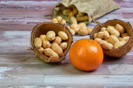 Peanuts lies in a coconut shell on a wooden table with orange tangerine fruit, healthy food.の写真素材