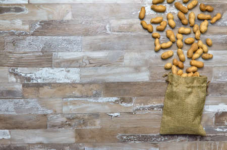 peanuts dropped out of a linen bag on a wooden table top view with place for text. Flat layの写真素材