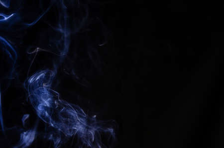 Abstract figure made of blue smoke on the left side of the frame on a dark background with place for text.Copy spaceの写真素材