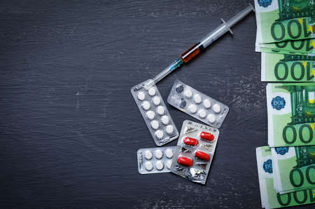 White and red pills, pills, drug in the package lie on a heap of euro money on a dark background top view, addiction problem.Copy pastの写真素材