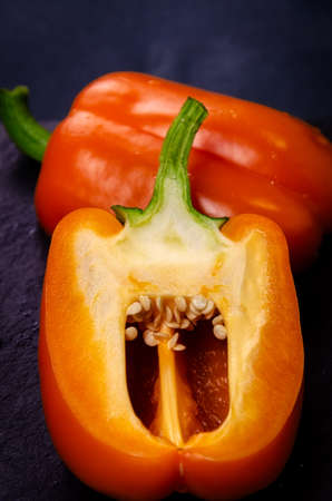 Orange sweet bell pepper cut in half, half closeup with seeds on a dark background, agriculture.Cutawayの写真素材
