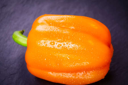 Orange sweet bell pepper with drops of water close-up on a dark background. Vegetable, agriculture.の写真素材