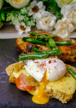 Breakfast on a black slate blackboard. Croutons with cheese, sausage, poached egg, green green beans. Vertical, close-up.の写真素材