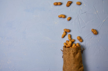 peanuts dropped from a linen bag on a blue textural background top view, place for text, copy space