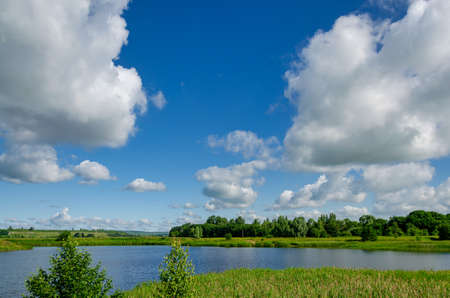 Big white clouds float over a lake in a forest on a blue sky, nature traveling on isolationの写真素材