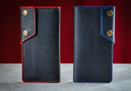 Two mens wallets longer made of genuine black leather handmade with a red and blue edge and two buttons close-upの写真素材