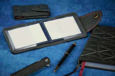 Handmade product made of genuine leather, graphite color, ID cover on a blue background with a black notebook, pen, lighter. Empty space for text and photos.の写真素材
