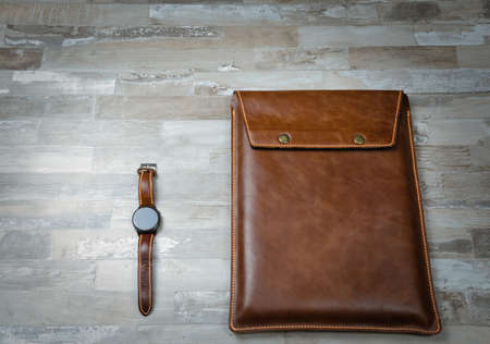 Handmade brown leather laptop case on a wooden table with a black clock. Top view, flatlay. Place for text.の写真素材