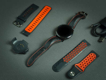 Wrist round sports smart watch, red two silicone straps, charger on a dark background and time on the dial.の写真素材