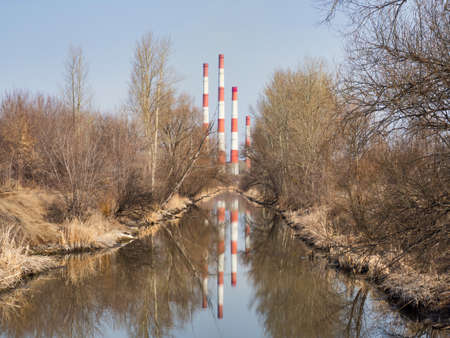 Water channel from a plant producing electricity, pipes in water reflection, trees without leaves on a sunny dayの写真素材