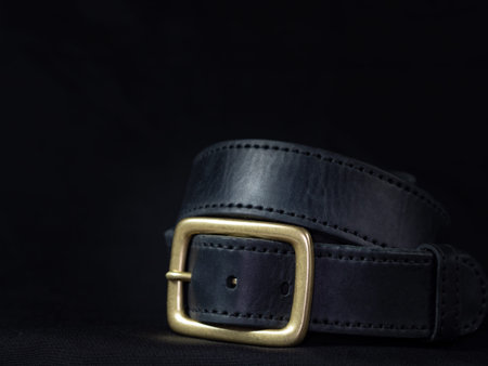 Mens black leather belt with heavy duty brass buckle on dark background free space for text