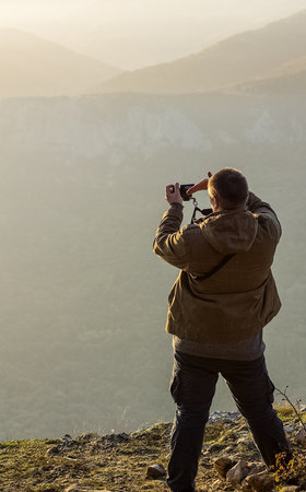 The man is on top of the mountain and takes pictures of the landscape of mountains and autumn forest.の写真素材