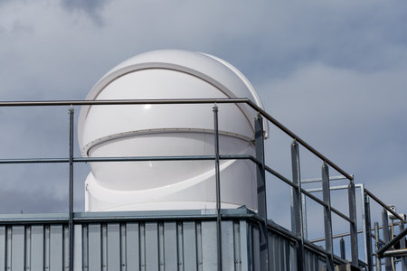 A beautiful view of an observatory dome with a white exterior and metal railings under a cloudy grey sky.の写真素材