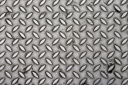 Close-up shot of a textured metal surface. The pattern consists of raised, elongated oval shapes arranged diagonally. The color is primarily gray.の写真素材