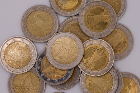 Close-up of scattered 2 Euro coins on a light gray surface, showing various national designs and the...