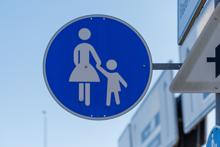 A blue circular sign with white figures of a woman and child holding hands against a clear blue sky.の写真素材