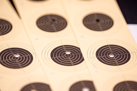 A close-up, angled view of multiple light brown paper targets with black concentric circles and numbering. Some targets have bullet holes.の写真素材