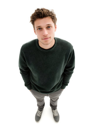 A young man with curly hair and a dark green sweater is standing with his hands in his pockets, captured from a high angle view for use in stock photography.の素材