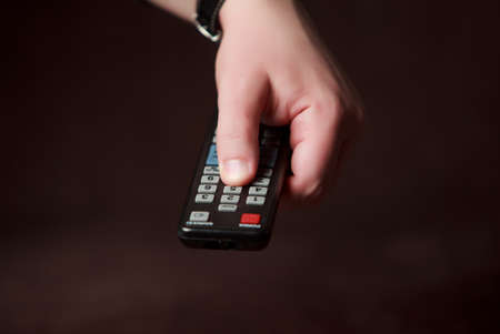 Hand holding a remote control over dark background selective focusの写真素材