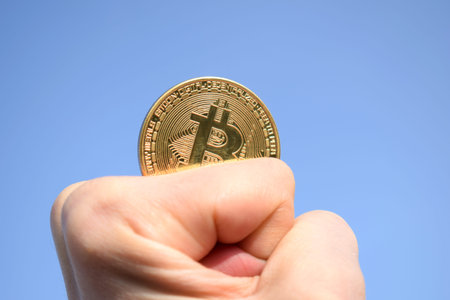 Hand holding golden bitcoin coin on blue sky background. Cryptocurrency. Golden coin.