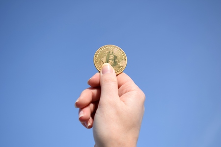 Bitcoin coin in hand, blue sky backgroundの写真素材