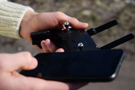 Remote control and smartphone in male hands. A man holding a transmitter and piloting some vehicles. A drone, radio controlled car or helicopter is running. Leisure, hobby, entertainment concept.の写真素材