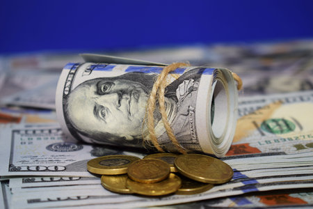 A roll of dollars on the background of scattered hundred dollar bills and various coins. Currency...
