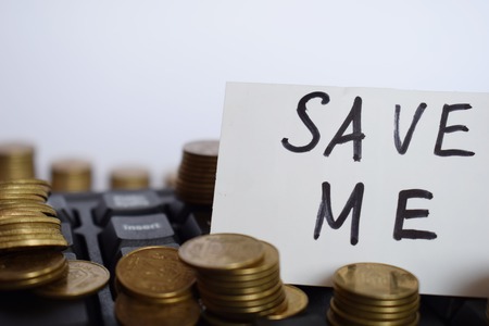 The inscription Save me on a white piece of paper on the keyboard surrounded by coins, the concept of saving moneyの写真素材