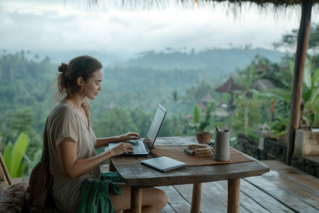 Young woman working on a laptop in a cafe with a mountain viewの素材