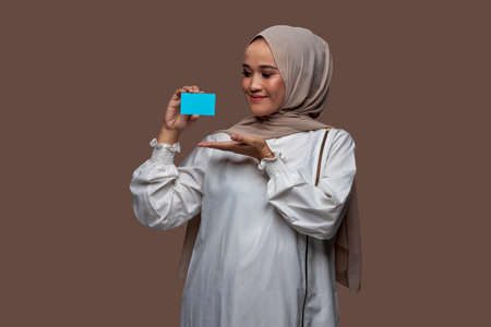 Beautiful hijab woman holding and showing plain credit card, plain business card, suitable for mock upの写真素材