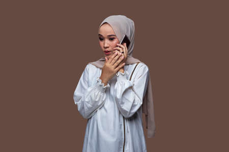 Beautiful woman in hijab is holding a mobile phone and showing it forwardの写真素材