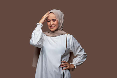 Young indonesian woman in hijab holding head with dizzy expression, stress, headacheの写真素材