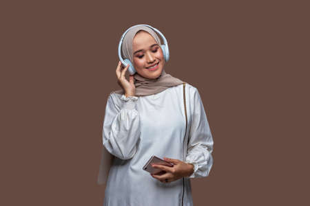 Beautiful woman in hijab is listening music from her cellphone using wireless headphones while closing her eyesの写真素材