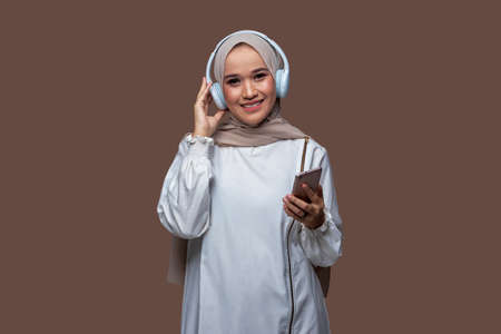 Indonesian woman in hijab posing wearing headphones and holding cellphoneの写真素材