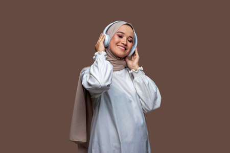 Indonesian women wearing hijab using wireless headphones are enjoying listening to music while closing their eyesの写真素材