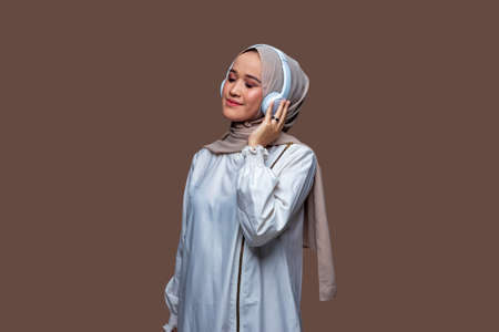 Portrait of women wearing hijab using wireless headphones are enjoying listening to music while closing their eyesの写真素材
