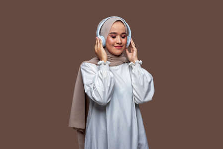 Women wearing hijab using wireless headphones are enjoying listening to music while closing their eyesの写真素材
